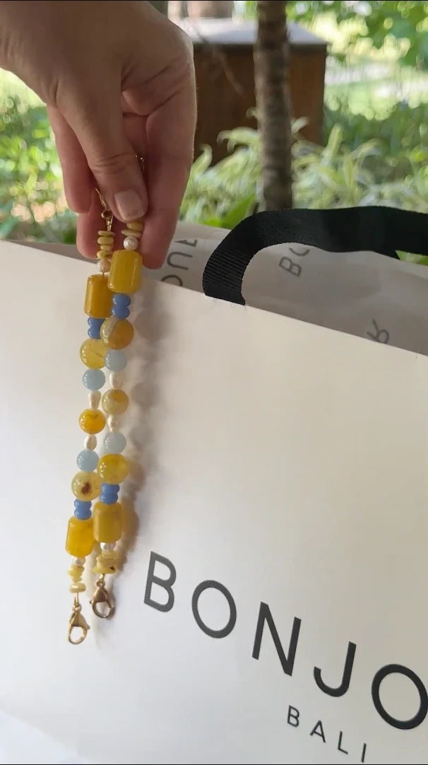 Un paio di spalline gialle e blu, tenute sopra una borsa Bonjour Bali