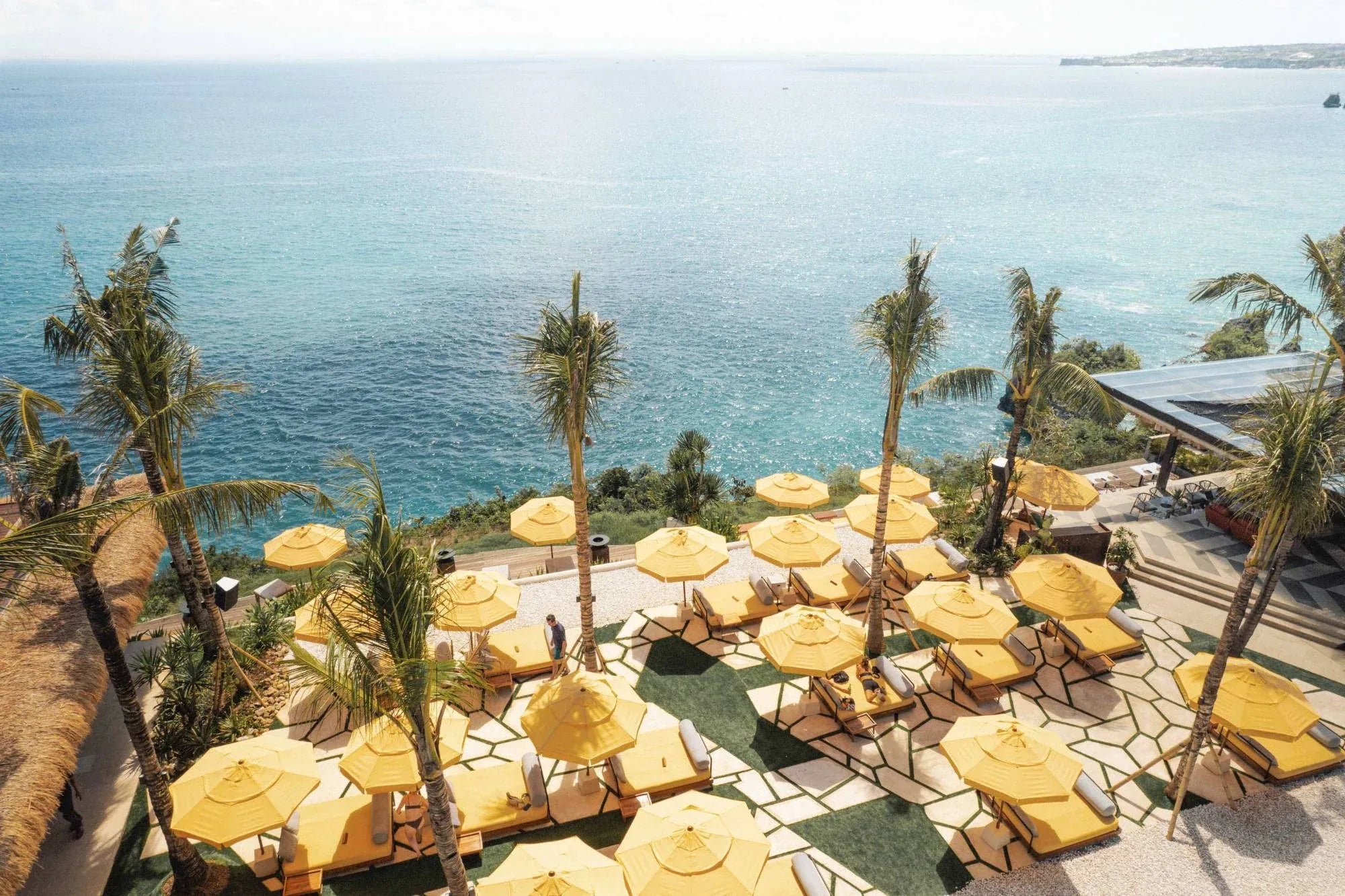 Ulu Cliffhouse vista dall'alto: ombrelloni gialli e lettini sulle scogliere di Uluwatu a picco sull'oceano