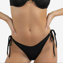Close-up of the black bikini waistband and side-tie detail, showcasing the smooth fabric texture and secure hardware for beach styling.