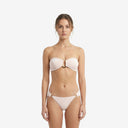 Front view of a model wearing a baby pink bandeau bikini set featuring a central gold metal ring and tango-style bottoms