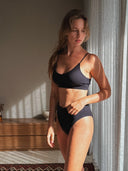 Woman in a white bra and panties Cotton Set Love Child Bali sitting on a couch holding a glass of water.