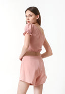 A female model wearing a pink sleeveless crop top with a tie-on strap and elastic on the waist