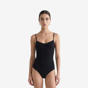 Front view of a model wearing a black contoured one-piece bodysuit with thin straps and a structured bust design.