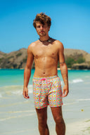 Front view of a model wearing Lollipop men's swim shorts featuring a vibrant pink and orange floral print on a green background with adjustable pink drawstrings.